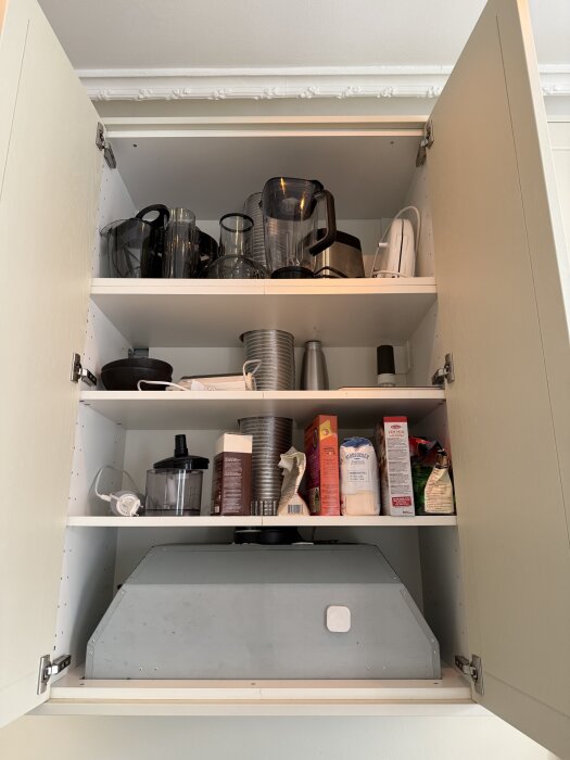 Öppna skåpdörrar med hyllor, visande köksföremål och ett ventilationsrör som blockerar utrymmet för en mikrovågsugn ovanför en köksfläkt.