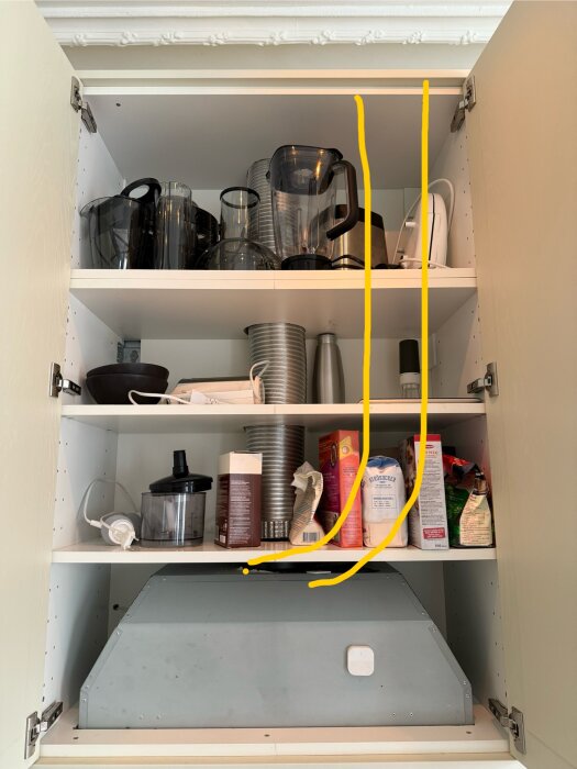 Köksskåp med köksfläktens rör som sticker ut, hindrar plats för mikro. Hyllan rymmer blandade ting, t.ex. matvaror och köksapparater.