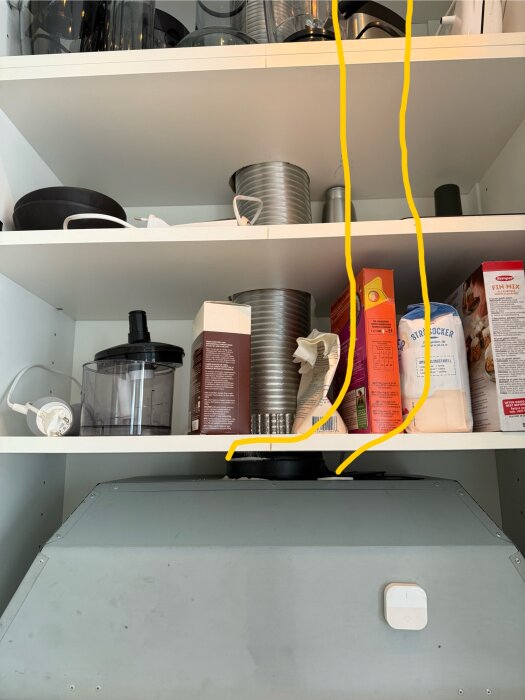 Kökshyllor med kokböcker och köksredskap. Ett ventilationsrör går genom hyllorna ovanför en inbyggd köksfläkt, vilket hindrar plats för en mikrovågsugn.