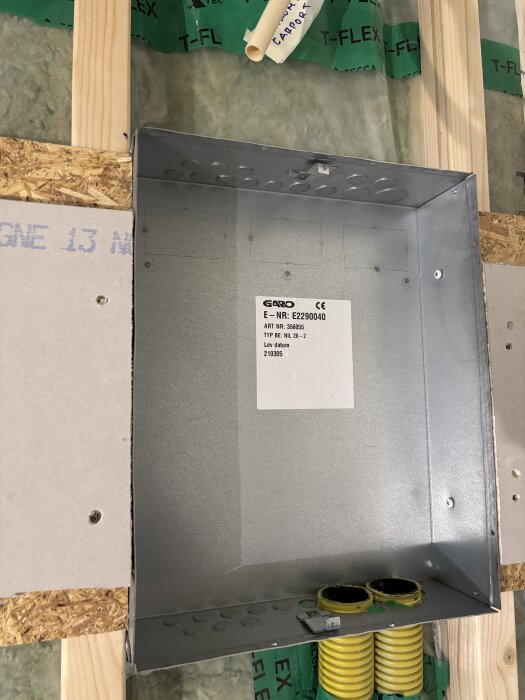 Elskåp installerat i vägg med etikett "Garo" och artikelnummer. Bakgrunden visar trä och isolering.