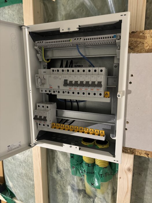 Elcentral med säkringar installerad inuti en vägg, med gula ledningar och märkningar från Garo.