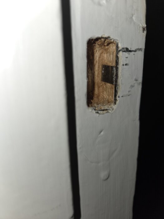 Äldre innerdörrkarm med urgröpt trä där låsets del syns, problem med att stänga och låsa dörren.