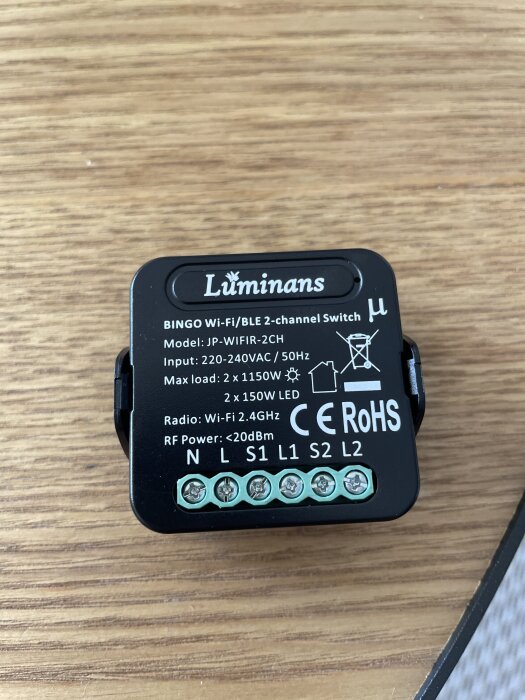 Luminans Wi-Fi/BLE 2-kanalsdimmer med anslutningsportar och specifikationer på framsidan, liggande på en träyta.