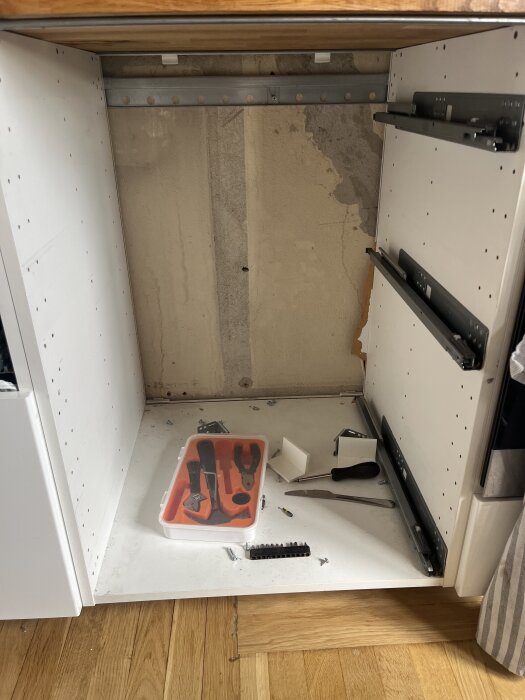 Ett tomt köksskåp utan stomme med verktyg som hammare och skruvmejslar placerade på bottenplattan av skåpet.