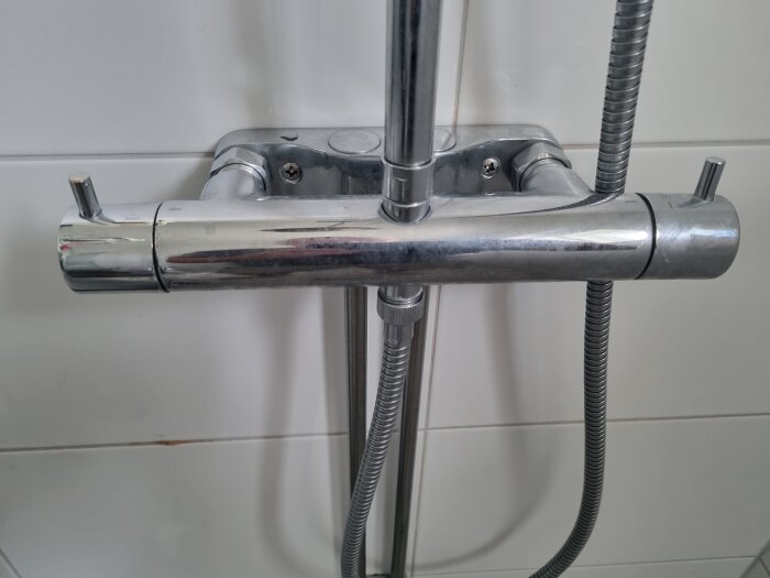 Kromfärgad duschblandare monterad på vita kakelplattor med ansluten duschslang.