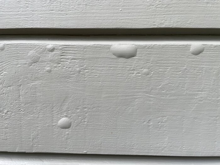 Närbild av en målad träfasad med färgbubblor som synts efter målning, vilket kan bero på kvarstående olja eller träets kondition.