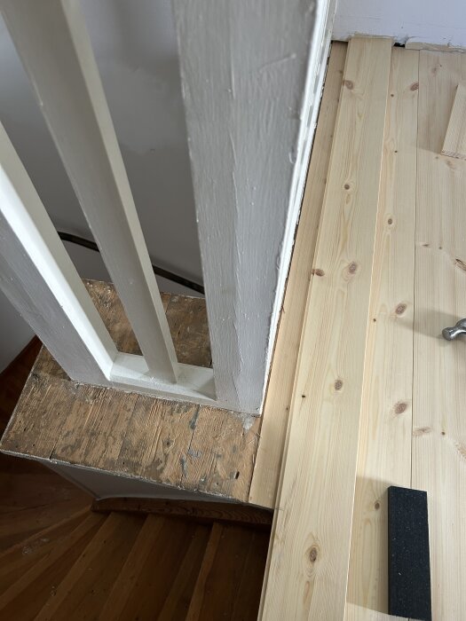 Trätrappa med oavslutat räcke ovanför, mot nytt golv av trä. Fråga om designlösningar för att förbättra utseendet runt räcket.