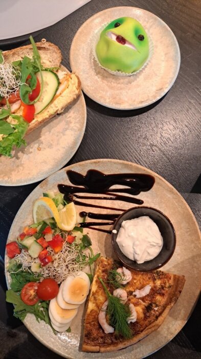 Sallad och laxpaj med dill och räkor, baguette med kycklingcurry, och en grön marsipanbakelse på ett bord.