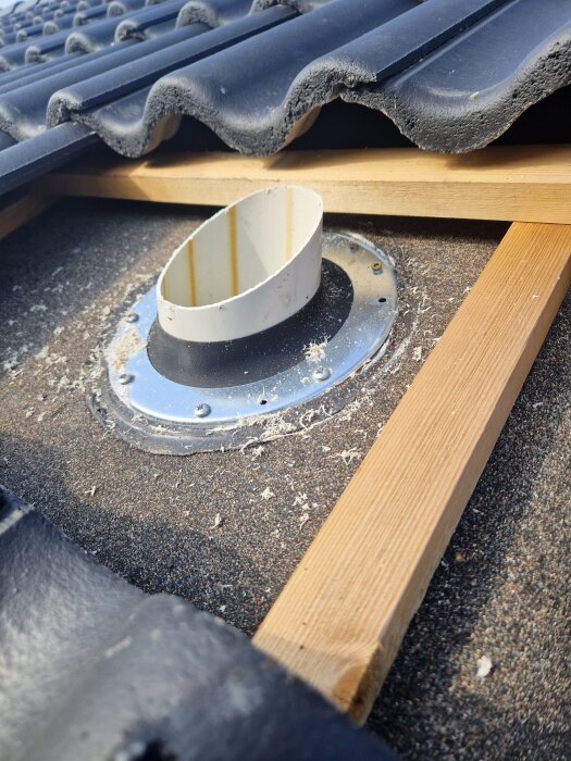 Avloppsluftare monterad på tak med underlagspapp, del av svart takpanna och träreglar syns runt ventilen.