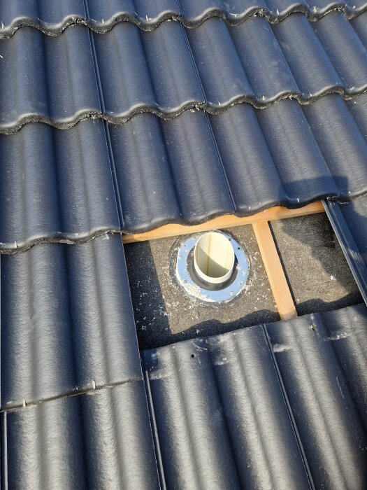 Tak med svarta pannor, delvis avtäckt för att visa ett avloppsrör som sticker upp genom undertaket. Runt röret syns en metallmanschett.