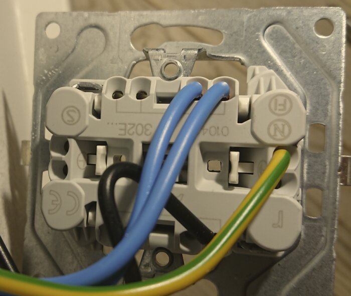Väggkontakt med två blå kablar, en svart och en gul-grön jordkabel, kopplade till terminalklämmor.