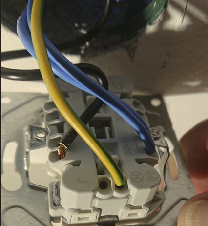 Elektrisk vägguttag med blå, gul-grön och svart kabelanslutning, visas delvis monterad i väggen.