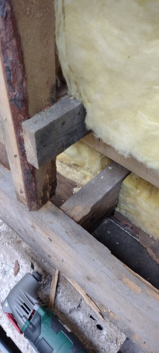 Byggprojekt med träregel på grundmur, isolering och del av elverktyg synligt. Regelmätning och reparation är pågående.