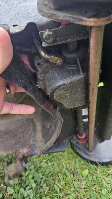 Närbild av gräsklippardel där kopplingen snurrar fritt runt axeln, med handen som pekar på området under remskyddet.