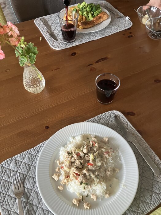 Tallrik med asiatisk kycklingfärs och ris, bredvid stekt lax med pommes och broccoli. Ett glas hälls upp.