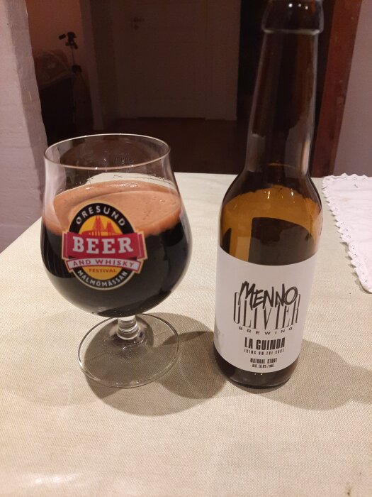 Glas och flaska av en stout från Menno Olivier Brewing, märkt som La Guinda, placerad på ett bord.