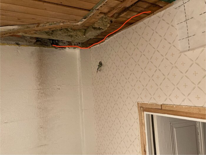 Öppnad takkonstruktion med rött streck som visar planerad plats för spirorör i badrumsrenovering, trasig isolering syns.
