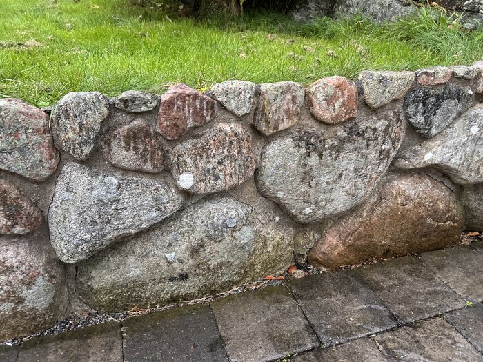 Stenmur av oregelbundna stenar framför en gräsmatta, del av ett byggprojekt.