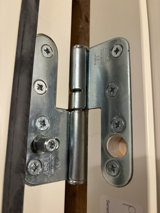 Assa gångjärn på ny ytterdörr, uppvisar justeringsutmaning; nära tröskel nedtill, flera millimeter överskott upptill.