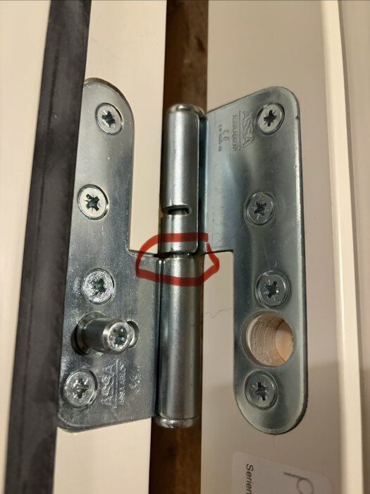 Dörrgångjärn i närbild med en röd markering mitt på skruvarna.