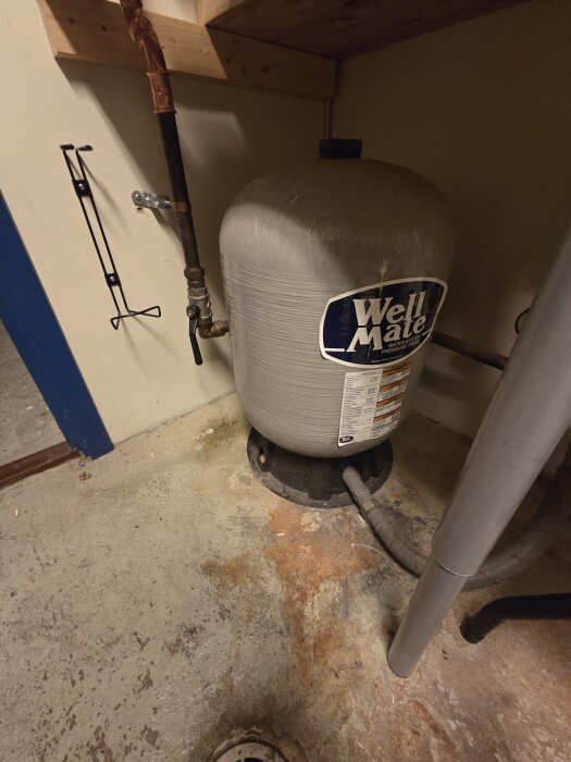 Trycktank märkt "Well Mate" installerad inomhus, synlig ledning och ventil, del av ett vatten- eller värmesystem.