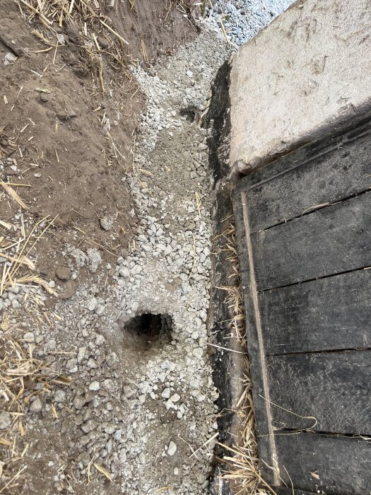 Grushög vid en betongplatta med ett råtthål bredvid en träram.