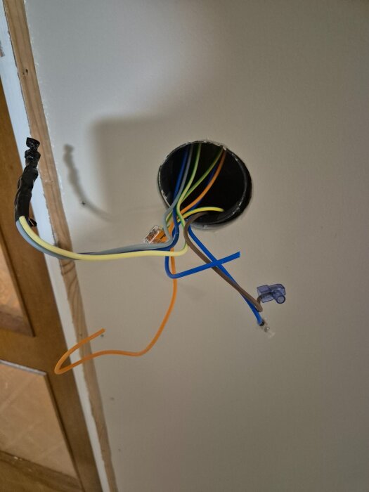 Elinstallation med flera kablar i olika färger som hänger från en dosa i en vägg; brun, blå, jord, orange och grå syns.