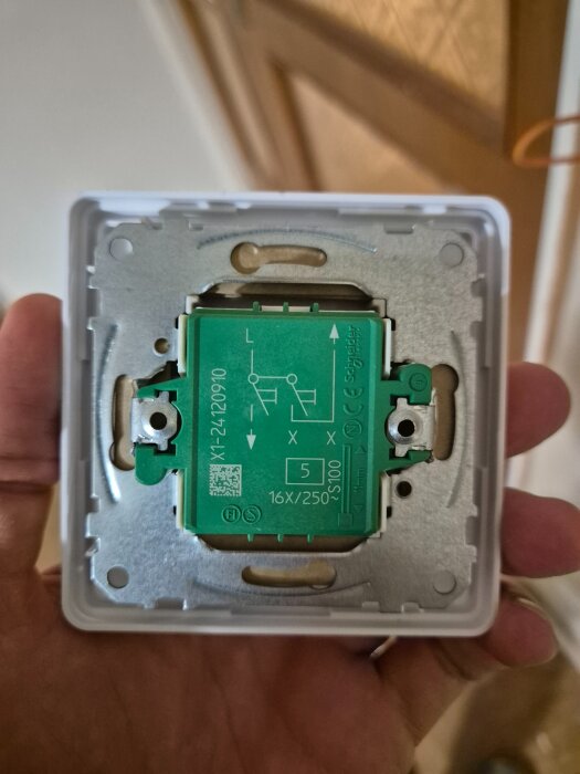 En hand håller i en strömbrytare från Schneider med en grön baksida som visar anslutningar och symboler.