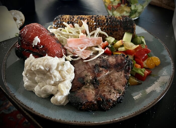 Grillad fläskkarré med grillad majs, ostfylld paprika, kålsallad, potatissallad och sommarsallad på tallrik.