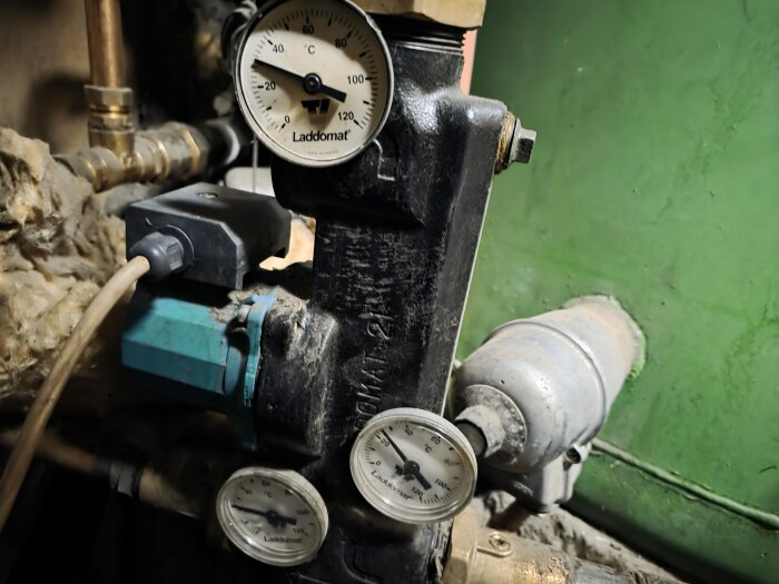 Temperaturmätare på Laddomat-enhet, med rör och ledningar i bakgrunden, används i uppvärmningssystem.