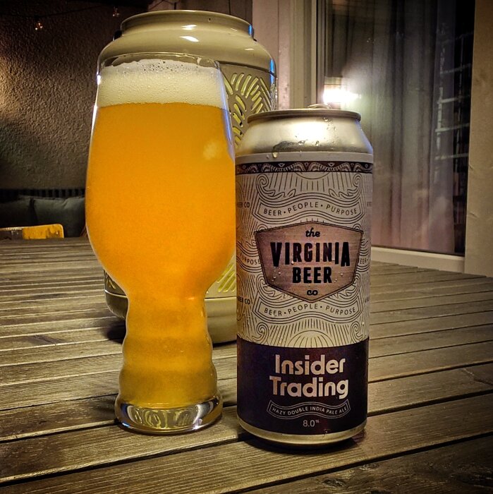 En ölburk märkt "The Virginia Beer Co. Insider Trading" bredvid ett fyllt ölglas på ett bord.