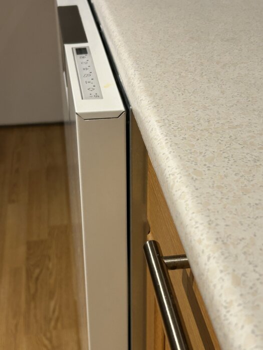 Närbild på diskmaskinens framsida med luckan utdragen, livad med bänkskivan bredvid en kökslucka med metallhandtag.