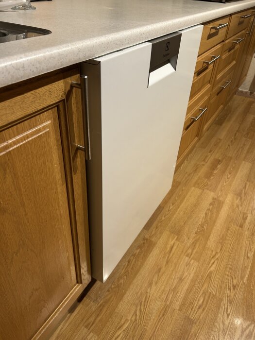 Inbyggd diskmaskin i kök med träskåp och laminatbänkskiva, maskinen är intryckt och nivå med skåpen.