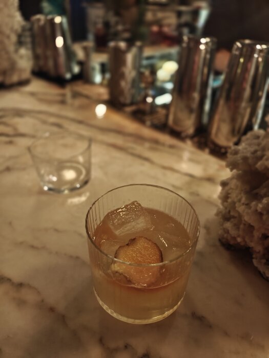 Cocktail med iskuber och ingefärsskiva i glas på marmorbord.