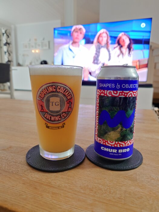 Öl från Toppling Goliath och Shapes & Objects i glas och burk på bord, TV i bakgrunden.