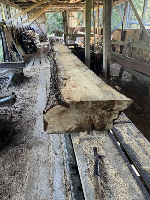 Sågade plankor i en träverkstad, fyllda på virkesförrådet, med verktyg och träspån synliga på golvet.