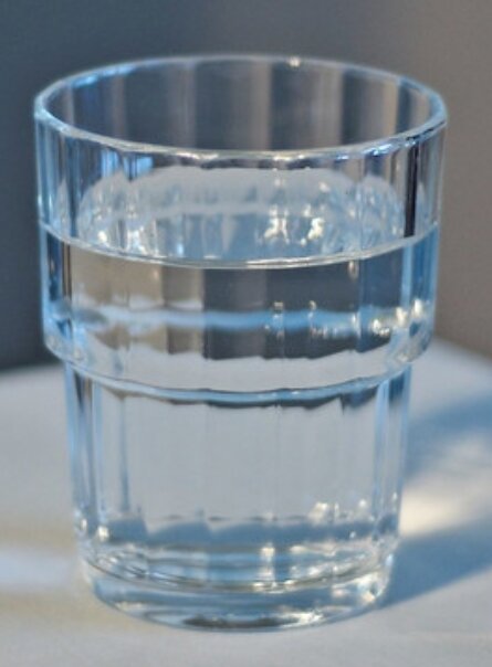 Ett genomskinligt glas fyllt med vatten står på ett bord.