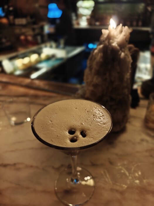 Espresso Martini serverad i ett cocktailglas på en marmorbänk med ett tända ljus i bakgrunden.