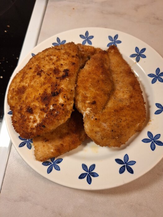Panerad kycklingsnitzel på en vit tallrik med blå blommor, lagad som del av veckans frysmat.