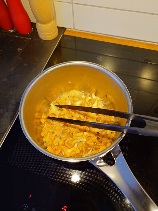 Svamp förvälls i en kastrull på en induktionshäll. En pincett används för att röra om svampen.
