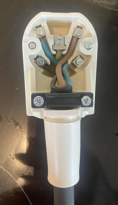 Elektrisk kontakt med fyra ledare anslutna: blå, brun, grön/gul och svart. Skruvterminaler och en vit plastkåpa synliga.