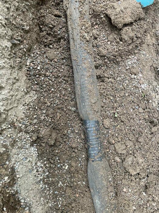 Grävd jord med en slang som har svart tejp runt en skarv. Slangen ser ut att vara kopplad till ett avlopp vid en husvägg.