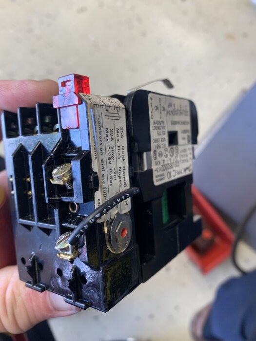 Svart Danfoss motorbrytare med motorskydd, röd knapp synlig, hållen i hand, på en ljus bakgrund, använd i bygg- och renoveringsprojekt.