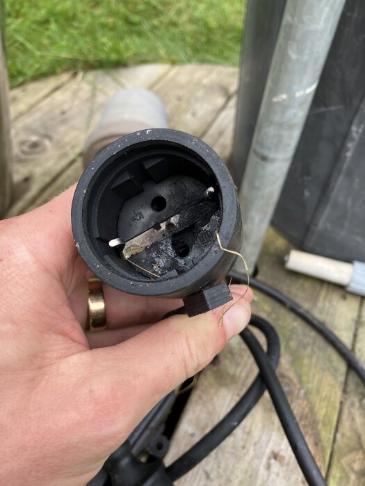 Närbild på en hand som håller en bränd och delad elektrisk kontakt, kopplad till en pump.