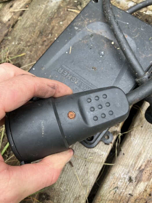 Svart kontakt med synligt rostigt område på en träyta, hållen av en hand, relaterad till pumpproblem.