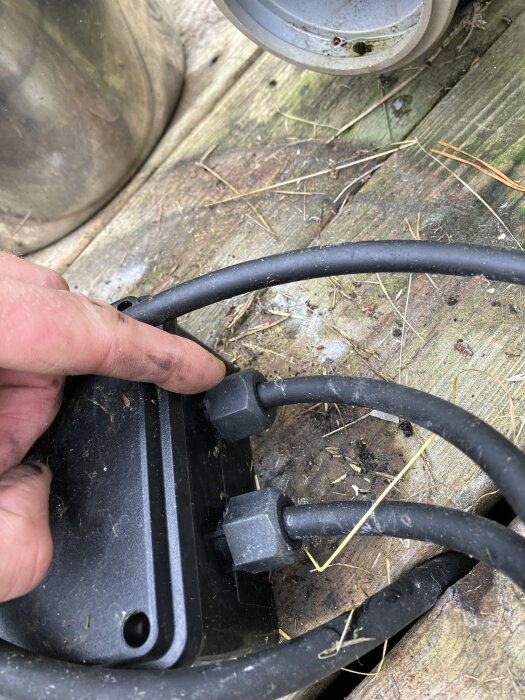 Trasig pumpkontakt med brända delar och separerade kablar på trädäck, indikerar fukt- och användarslitage.