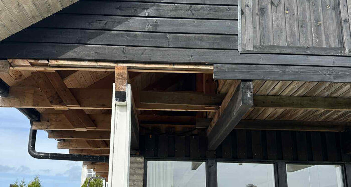 Trätak under konstruktion där mellanbjälkar och innertakets träpaneler syns. En metallskena är placerad tvärs över de synliga bjälkarna.