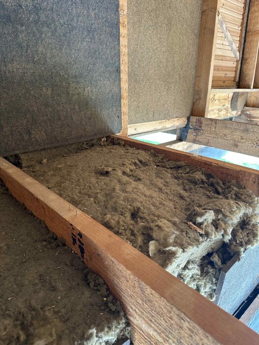 Isolering placerad mellan träbjälkar i en halvt färdig kattvind, med träpanel och isolerskivor synliga på väggarna.