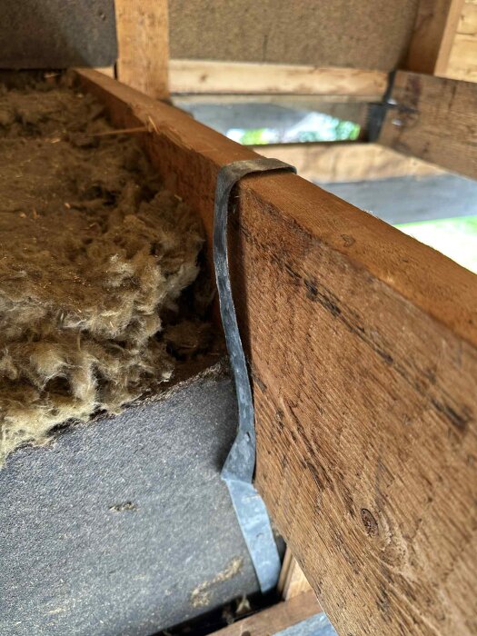 Metallremsa fäst vid träbjälke ovanpå isoleringsmaterial i en husvind.