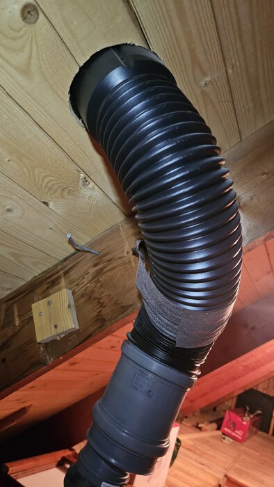 Svart flexrör för avloppsavluftning på vind, delvis lindat med tejp. Röret har en böjning som kan ha orsakat sprickor och kondensläckage.